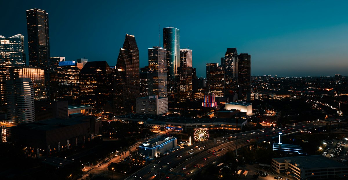Aerial view of downtown Houston at night, with lit office towers above a freeway and the convention district.