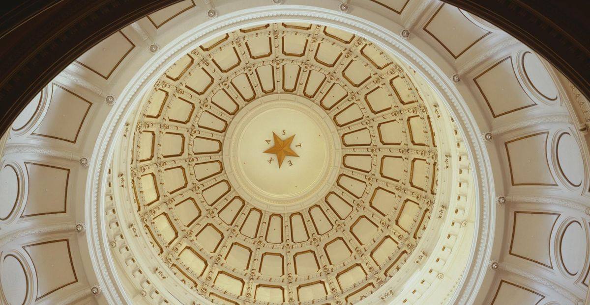 Looking up into the Texas Capitol dome in Austin, with the gold Lone Star and the letters T-E-X-A-S at its center.