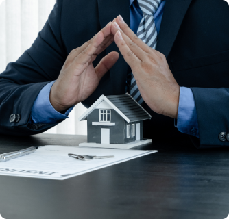 A person in a business suit framing a small model house with their hands in the shape of a protective roof.