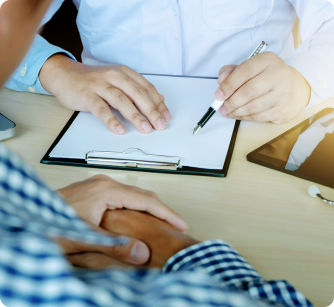 A person in a white shirt holds a pen over a blank clipboard while sitting across from a client in a checkered shirt.