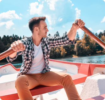 A man in a plaid shirt rowing a red and white boat on a sunny lake.