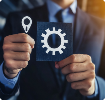 A person in a business suit holding two cards, one with a gear icon and the other with a location pin symbol, suggesting settings or operations related to location