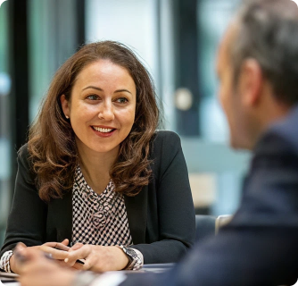 A smiling professional woman with brown hair engaging in a conversation during a business meeting.