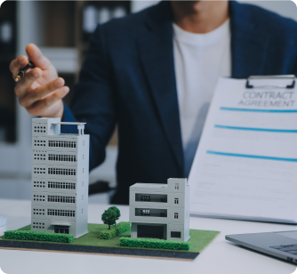 A professional in a blazer points toward an architectural model of a high-rise building while holding a contract agreement.