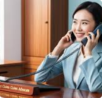 A smiling female claims advocate talking on a desk phone in a professional office.