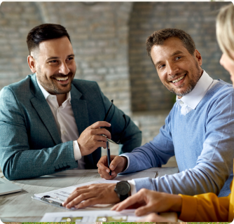 Two men in business attire smile and laugh during a positive meeting over paperwork