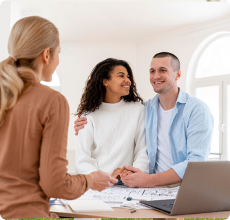 Two professionals in business attire sit at a glass table during a meeting. A woman in a light-colored suit is speaking and gesturing, while a man in a grey suit and tie looks at a laptop. The background is a blurred, modern office interior.