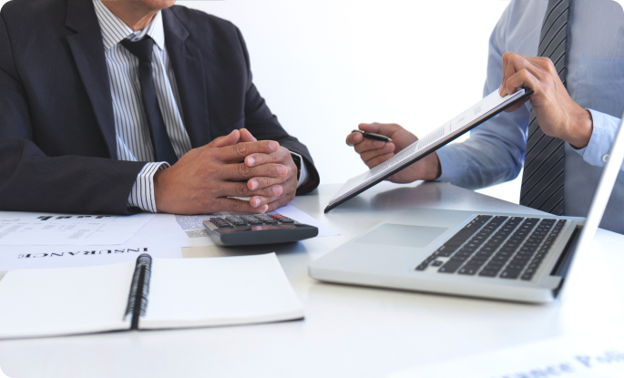 Two professionals in suits discussing insurance documents over a desk with a laptop and calculator.