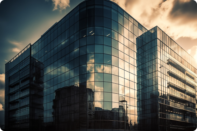 A low-angle shot of a modern glass skyscraper reflecting a cloudy sky and sunset light across its curved architectural facade.