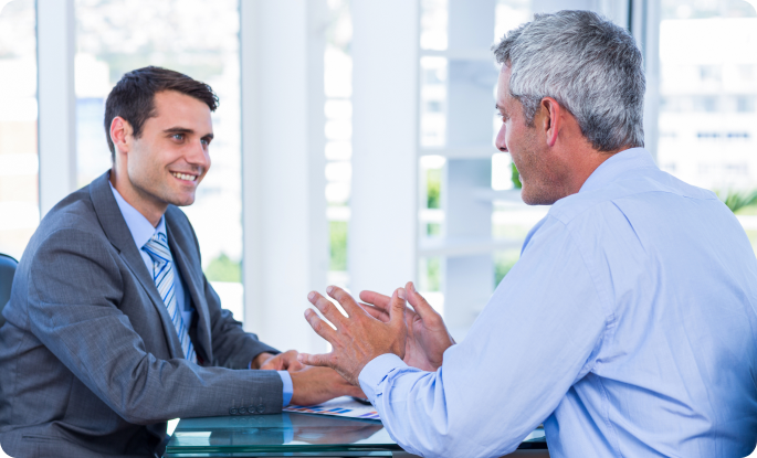 A younger businessman and an older executive discussing information on a tablet in a bright, modern office.