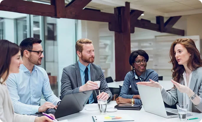 A diverse group of colleagues sits around a conference table engaged in an active business meeting.