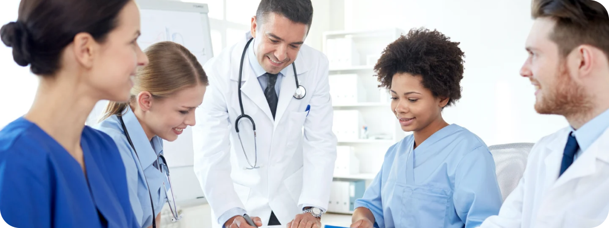 A diverse team of medical professionals, including a male doctor with a stethoscope and nurses in blue scrubs, smiling and collaborating over a document in a bright clinic.